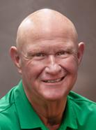 Bald man wearing a green polo shirt, smiling in front of a neutral background.